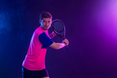 Raketli Padel tenisçi. Sahada raketli, neon renkli bir erkek sporcu. Spor konsepti. Bir spor uygulaması ya da bahis sitesi tasarımı için yüksek kaliteli bir fotoğraf indir