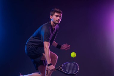 Raketli Padel tenisçi. Sahada raketli, neon renkli bir erkek sporcu. Spor konsepti. Bir spor uygulaması ya da bahis sitesi tasarımı için yüksek kaliteli bir fotoğraf indir