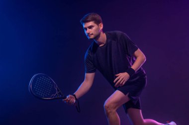 Raketli Padel tenisçi. Sahada raketli, neon renkli bir erkek sporcu. Spor konsepti. Bir spor uygulaması ya da bahis sitesi tasarımı için yüksek kaliteli bir fotoğraf indir