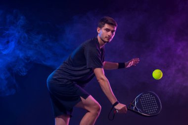 Raketli Padel tenisçi. Sahada raketli, neon renkli bir erkek sporcu. Spor konsepti. Bir spor uygulaması ya da bahis sitesi tasarımı için yüksek kaliteli bir fotoğraf indir