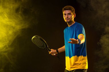 Raketli Padel tenisçi. Sahada raketli, neon renkli bir erkek sporcu. Spor konsepti. Bir spor uygulaması ya da bahis sitesi tasarımı için yüksek kaliteli bir fotoğraf indir