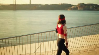 Zinde bir kadın gün doğumunda zarif bir şekilde dışarı uzanırken, arka planda çarpıcı bir köprü görülebilir.