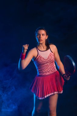 Raketli Padel tenisçi. Sahada raketi neon renkli genç bir sporcu kız. Spor konsepti. Bir spor uygulaması ya da bahis sitesi tasarımı için yüksek kaliteli bir fotoğraf indir