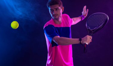 Raketli Padel tenisçi. Sahada raketli, neon renkli bir erkek sporcu. Spor konsepti. Bir spor uygulaması ya da bahis sitesi tasarımı için yüksek kaliteli bir fotoğraf indir