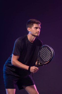 Raketli Padel tenisçi. Sahada raketli, neon renkli bir erkek sporcu. Spor konsepti. Bir spor uygulaması ya da bahis sitesi tasarımı için yüksek kaliteli bir fotoğraf indir