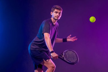 Raketli Padel tenisçi. Sahada raketli, neon renkli bir erkek sporcu. Spor konsepti. Bir spor uygulaması ya da bahis sitesi tasarımı için yüksek kaliteli bir fotoğraf indir