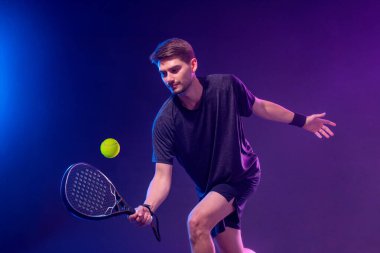 Raketli Padel tenisçi. Sahada raketli, neon renkli bir erkek sporcu. Spor konsepti. Bir spor uygulaması ya da bahis sitesi tasarımı için yüksek kaliteli bir fotoğraf indir