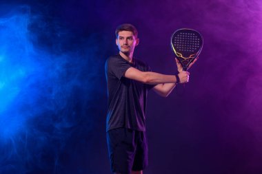 Raketli Padel tenisçi. Sahada raketli, neon renkli bir erkek sporcu. Spor konsepti. Bir spor uygulaması ya da bahis sitesi tasarımı için yüksek kaliteli bir fotoğraf indir