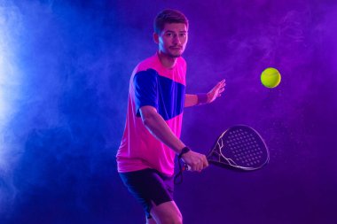 Raketli Padel tenisçi. Sahada raketli, neon renkli bir erkek sporcu. Spor konsepti. Bir spor uygulaması ya da bahis sitesi tasarımı için yüksek kaliteli bir fotoğraf indir