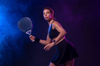 Raketli Padel tenisçi. Sahada raketi neon renkli genç bir sporcu kız. Spor konsepti. Bir spor uygulaması ya da bahis sitesi tasarımı için yüksek kaliteli bir fotoğraf indir