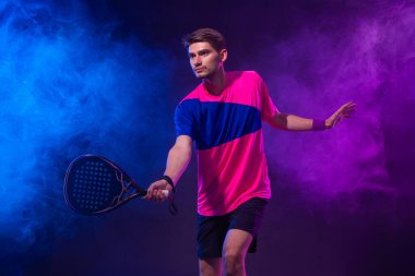 Raketli Padel tenisçi. Sahada raketli, neon renkli bir erkek sporcu. Spor konsepti. Bir spor uygulaması ya da bahis sitesi tasarımı için yüksek kaliteli bir fotoğraf indir