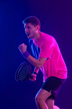 Raketli Padel tenisçi. Sahada raketli, neon renkli bir erkek sporcu. Spor konsepti. Bir spor uygulaması ya da bahis sitesi tasarımı için yüksek kaliteli bir fotoğraf indir