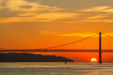 Lizbon 'daki 25 de Abril Köprüsü' nün Tagus Nehri üzerindeki günbatımı manzarası. Kartpostallar için mükemmel mıknatıslar seyahat rehberleri dergileri web siteleri ve turizm malzemeleri.