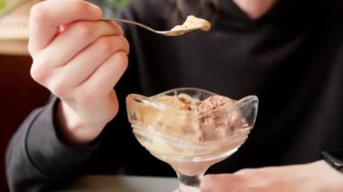 Eating vegan ice cream in cafe. Young woman with a spoon savouring dairy-free soy chocolate ice cream from sundae glass cup made of plant milk. Handheld close up shot