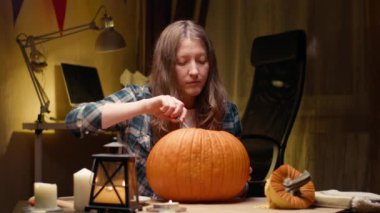 Preparing pumpkin for Halloween. Scooping out guts and seeds with spoon. Woman sitting and carving halloween Jack O Lantern pumpkin at home for her family.