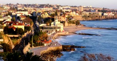 Sunset in Estoril. View from above on the Lisbon suburban coastline with people walking on promenade. Lisboa beach and ocean waves. Monte Estoril, Cascais, Portugal.