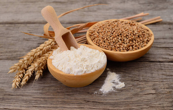 Spikelets, wheat grains and flour on wooden background.