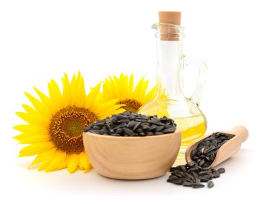 Cam şişedeki ayçiçeği yağı, tahta kase ve tohumlu kepçe ve beyaz arka planda izole edilmiş parlak sarı çiçekler. Organik gıda, sebze yağı ve sağlıklı beslenme kavramı