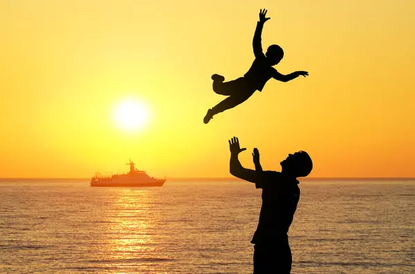 A father throws his son in his arms against the backdrop of sunset.
