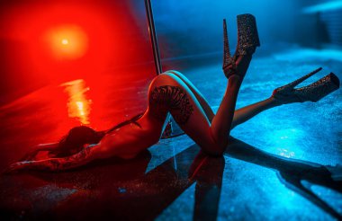 Young nude woman pole dancing in night club interior, tattoo on body