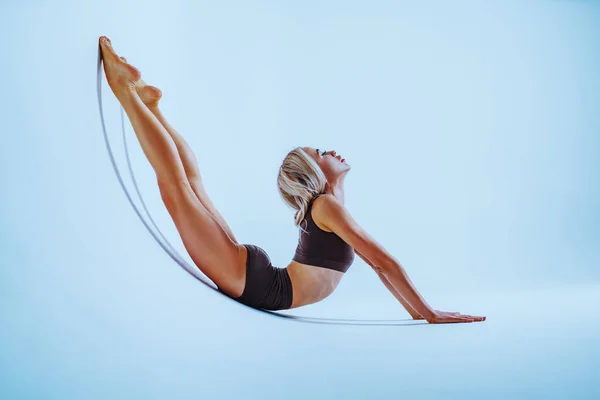 Young woman gymnast stretching on white wall background