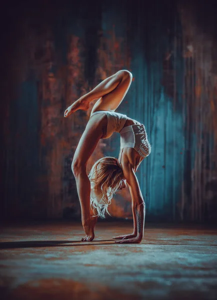 Young woman gymnast stretching on dark wall background
