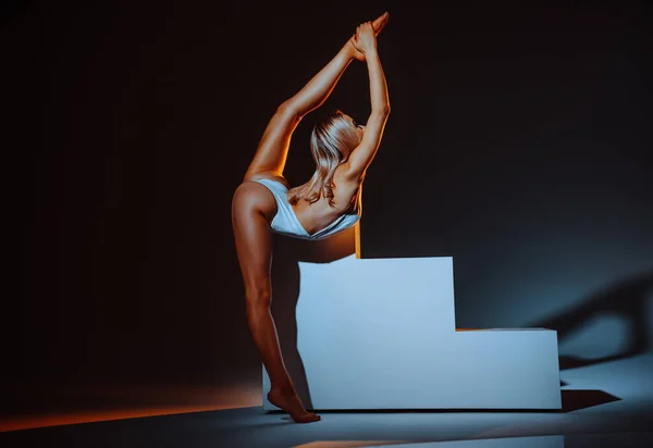 Young slim woman gymnast stretching in studio on dark background