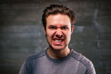 Young man angry portrait on gray wall background