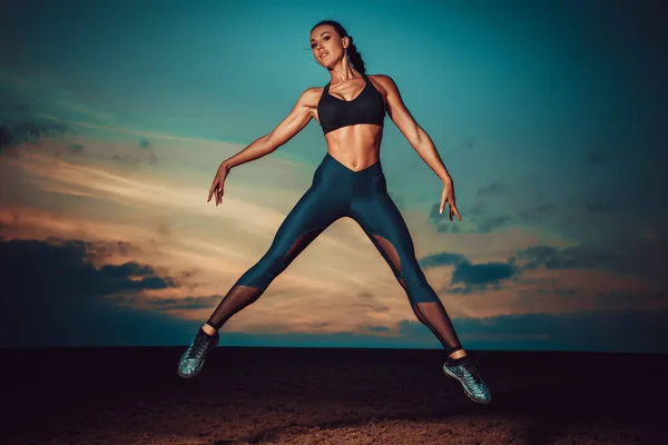 Young slim fitness woman jumping on twilight sky background