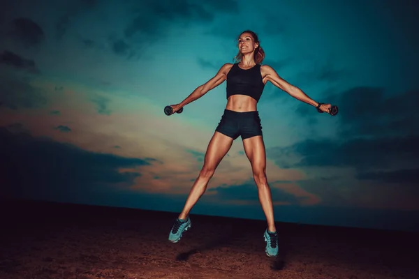 Genç Fitness Kadını Alacakaranlık Arka Planında Dambıllarla Zıplıyor — Stok fotoğraf