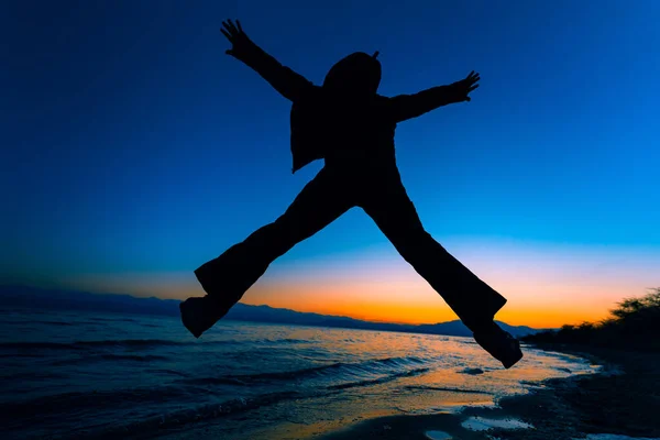 男は夕日の光で湖の背景シルエットにジャンプ — ストック写真