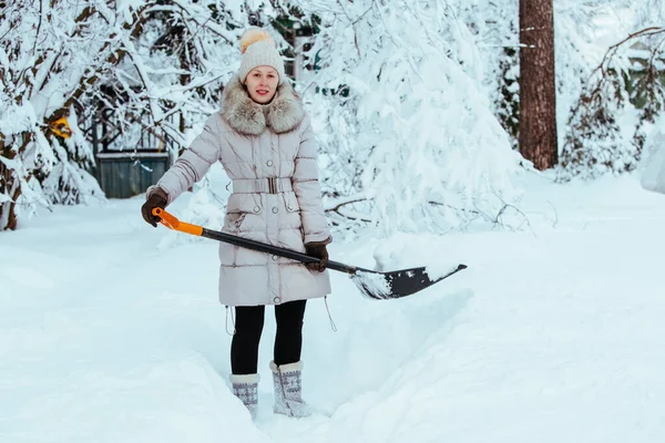 年轻女子在乡间用铲子清扫雪地的道路 — 图库照片