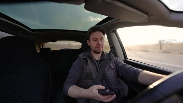 Mann Fährt Auto Und Schaut Bei Sonnigem Tag Auf Handy — Stockvideo
