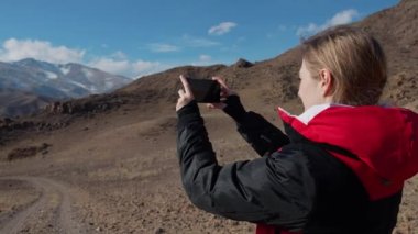 Genç bayan turist telefonda güzel dağ manzarası çekiyor.