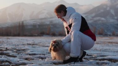 Genç bayan turist köpekle birlikte kış arka planında oturuyor.