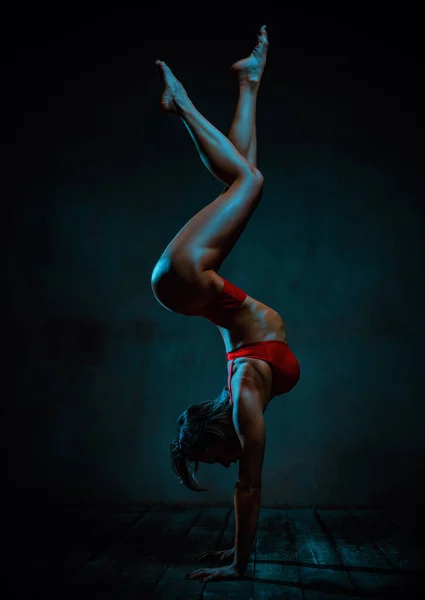 身穿红色内衣裤的年轻女运动员倒立在黑暗的背景下 — 图库照片