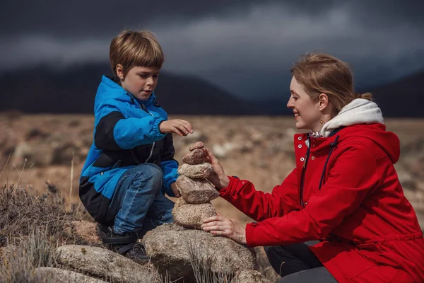 息子と一緒に山の中に石のピラミッドを構築する若い女性 — ストック写真