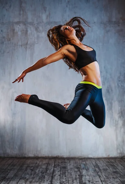 Молодая Стройная Спортивная Женщина Черной Одежде Прыгает Сером Фоне Стены — стоковое фото
