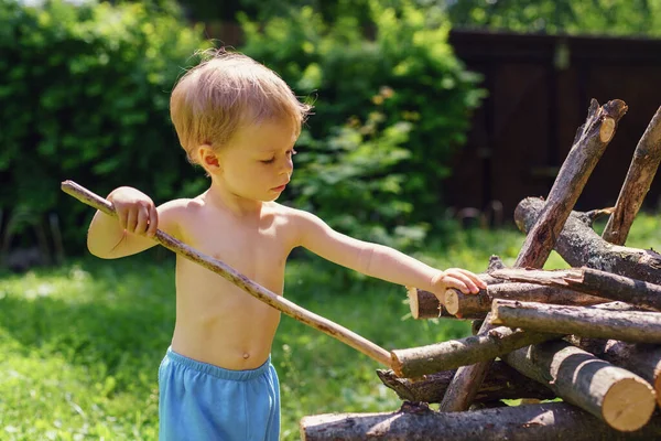 小さな男の子が庭の山に丸太を積み — ストック写真