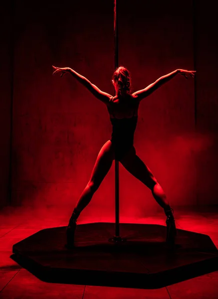 年轻女子撑杆跳着舞姿在演播室里 红色戏剧性的光芒 — 图库照片