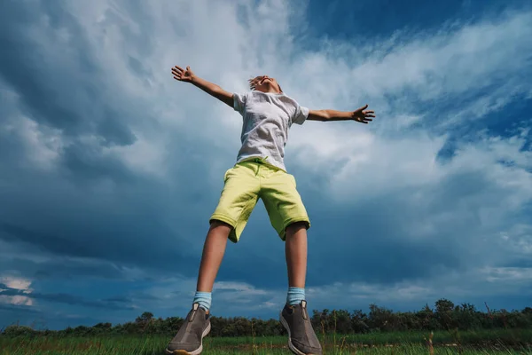快乐的男孩在蓝天背景的田野里跳跃 — 图库照片
