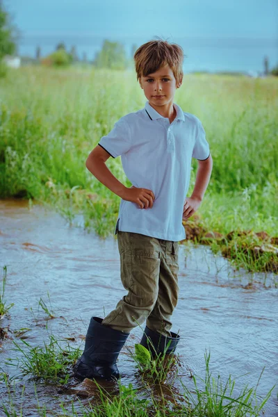 小川の真ん中にゴム製のブーツを着た少年が立っている — ストック写真