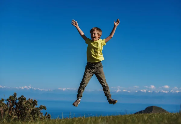幸せな少年は湖の背景に山にジャンプします — ストック写真