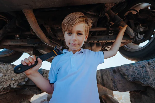 レンチで車の底の下に立つかわいい男の子の自動車整備士 — ストック写真