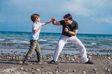 Baba, oğluna kumsalda dövüş sanatları öğretiyor.