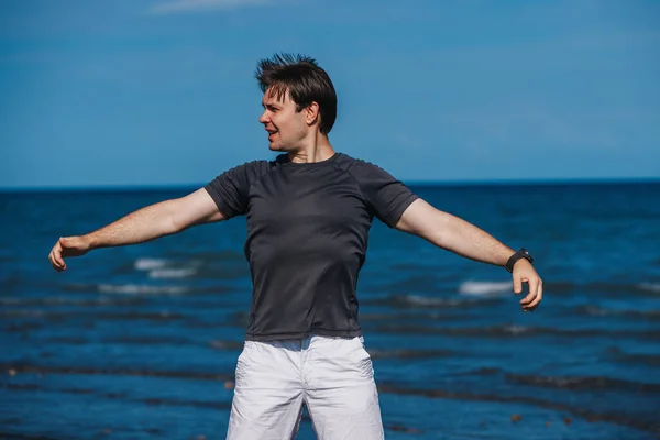 一个英俊的年轻人在刮风和热身的时候站在海滩上 — 图库照片
