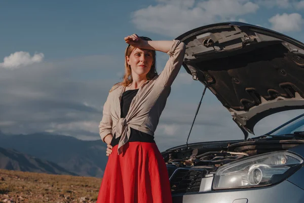山の背景で壊れた車の前に立っている疲れた若い女性 — ストック写真