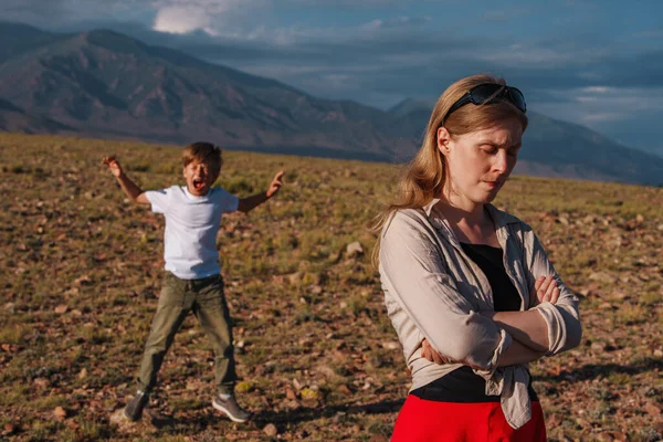 Frustrated mom turns away and her naughty son screaming on mountains background