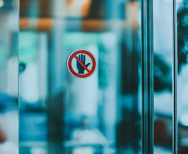 Stop hand warning icon for don\'t touch sign on glass door in modern public interior