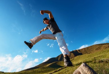 Yakışıklı atletik genç adam dağlarda zıplıyor.